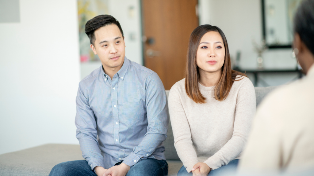 A young couple attends couples counselling in Calgary. They are sitting beside each other, facing the camera. The therapist is talking to them and facing away from the audience.