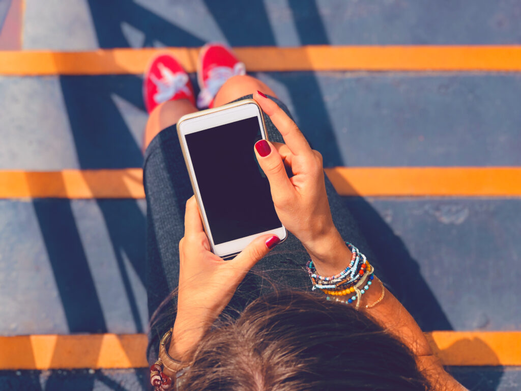 A woman scrolls on her phone in Calgary on a bright sunny day.